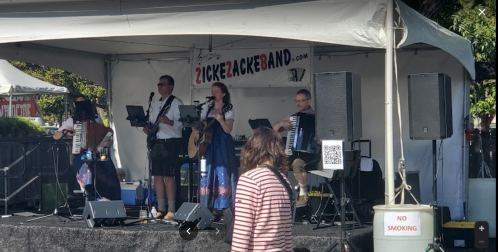 A band performs on stage under a tent, featuring musicians with various instruments, including an accordion and guitar.