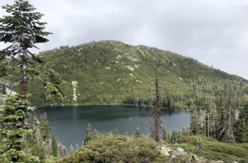 A serene lake surrounded by lush green trees and a mountainous landscape under a cloudy sky.