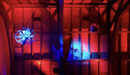 A dimly lit room with red and blue lighting, featuring a geometric sculpture and a disco ball hanging from the ceiling.