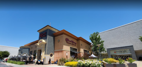 A shopping center featuring a restaurant and a Macy's, surrounded by colorful flowers under a clear blue sky.