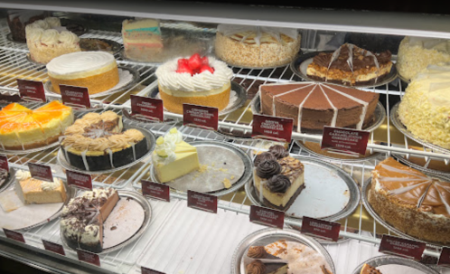A display case filled with various cakes and desserts, including cheesecakes, layered cakes, and chocolate treats.