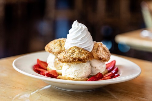 A dessert plate featuring three scoops of ice cream topped with whipped cream, cookies, and fresh strawberries.