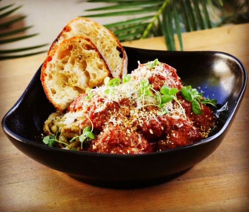 A black bowl filled with meatballs in marinara sauce, topped with herbs and served with a slice of toasted bread.