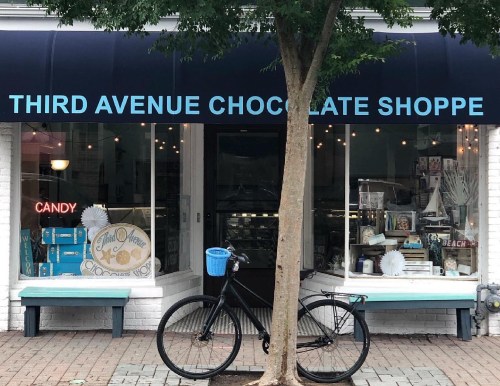 A storefront with a blue awning reading "Third Avenue Chocolate Shoppe," featuring a bicycle parked outside.