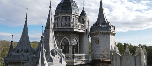 A tall, ornate castle with multiple spires and a domed roof, set against a cloudy sky.