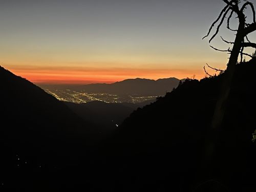 A serene mountain landscape at sunset, with vibrant orange and purple hues illuminating the sky over distant hills.