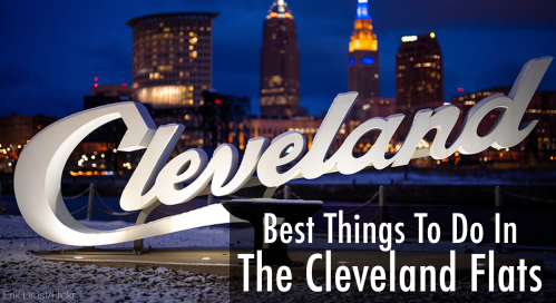A large "Cleveland" sign illuminated at night, with the city skyline and buildings in the background.
