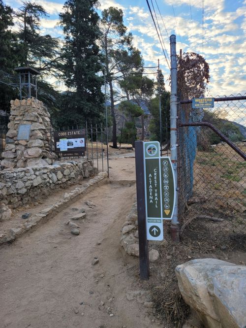 Entrance to Cobble Estate with a signpost and a stone monument, surrounded by trees and a fence.