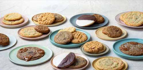 A variety of cookies displayed on colorful plates, including chocolate-dipped, peanut butter, and sprinkle cookies.