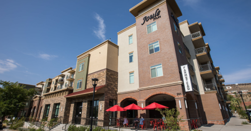 Modern multi-story building with a brick facade, featuring outdoor seating under red umbrellas and a sign for "Farmstead."