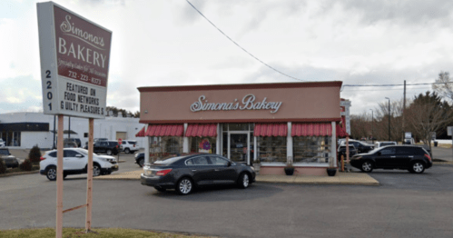 A bakery storefront with a sign reading "Simona's Bakery," featuring a parking lot and several cars outside.