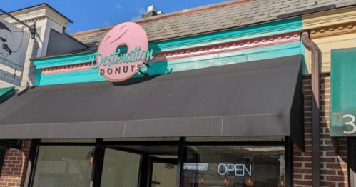 A storefront with a pink sign reading "Destination Donuts" and an "OPEN" sign in the window.