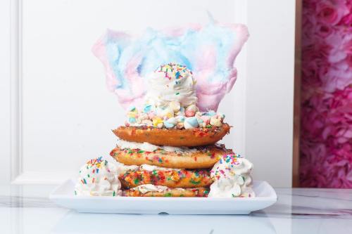 A colorful dessert tower featuring donuts, whipped cream, mini marshmallows, sprinkles, and cotton candy on top.