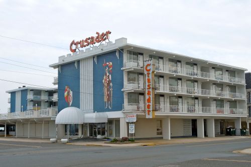 A three-story motel with a blue facade and large "Crusader" sign, featuring balconies and a mural on the side.
