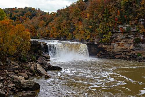 A waterfall cascades into a river, surrounded by autumn foliage and rocky cliffs.
