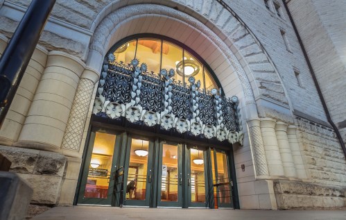 Entrance of a historic building featuring ornate architectural details and decorative floral elements above the doors.