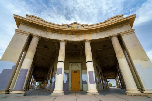 Abandoned building with tall columns and a weathered facade under a cloudy sky.