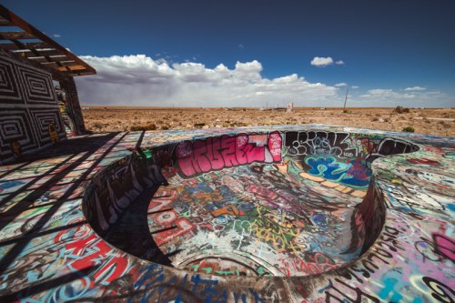 A colorful, graffiti-covered concrete structure in a desert landscape under a blue sky with scattered clouds.