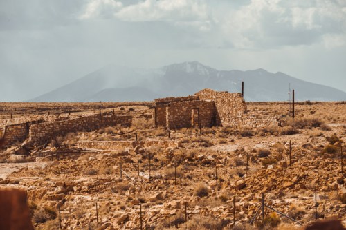 Ruins of a stone structure in a barren landscape, with mountains in the background under a cloudy sky.