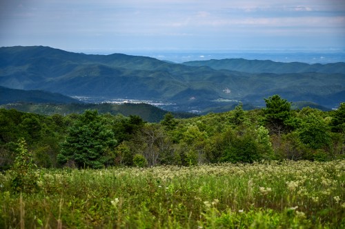 A panoramic view of rolling green mountains under a cloudy sky, with a valley and distant town visible below.