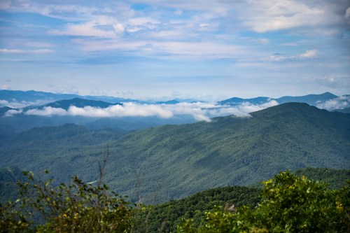 A panoramic view of lush green mountains under a cloudy sky, with layers of hills fading into the distance.