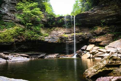 A serene waterfall cascades into a tranquil pool, surrounded by lush greenery and rocky cliffs.