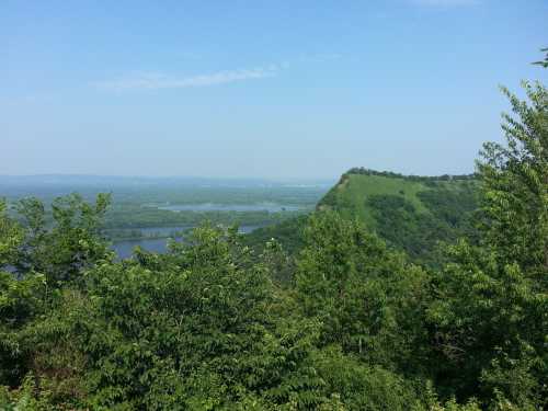 A scenic view of lush green hills and a river valley under a clear blue sky.