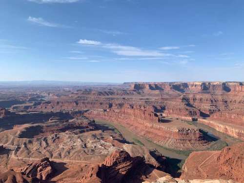 A panoramic view of a vast canyon landscape with red rock formations and a winding river under a clear blue sky.