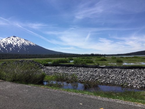 A scenic view of a snow-capped mountain beside a lush green landscape and a winding river under a blue sky.