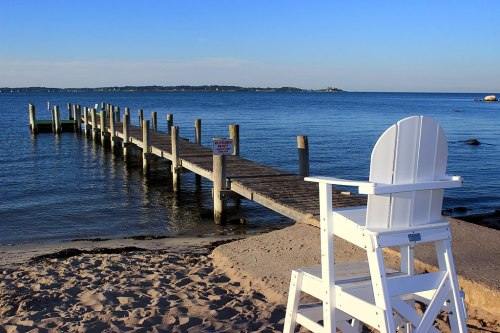 A wooden lifeguard chair on the beach, overlooking a calm sea and a long wooden pier extending into the water.