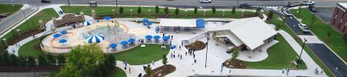 Aerial view of a park featuring a swimming pool, umbrellas, and a pavilion, with people walking around.