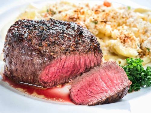 A perfectly cooked steak, sliced to reveal a juicy pink center, served with creamy pasta and a sprinkle of herbs.