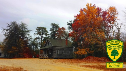 A rustic cabin surrounded by vibrant autumn trees at Double Trouble State Park, with a park logo and date in the corner.
