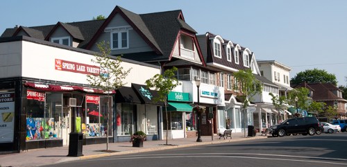 A sunny street view of shops with colorful storefronts and trees lining the sidewalk.