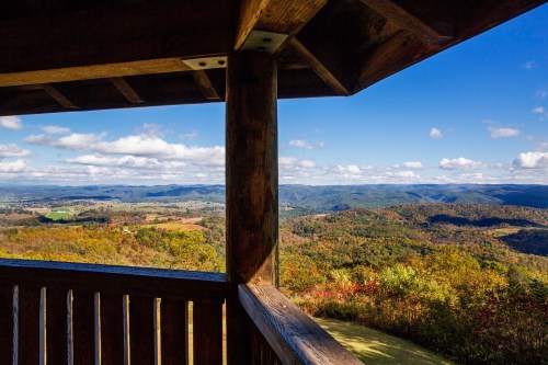 Scenic view from a wooden lookout, showcasing rolling hills and a vibrant autumn landscape under a blue sky.