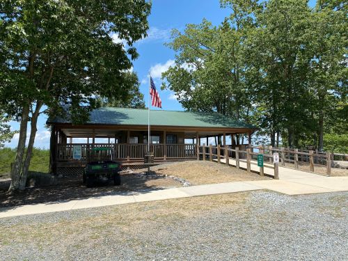 A wooden pavilion with a green roof, surrounded by trees, featuring an American flag and a gravel path.