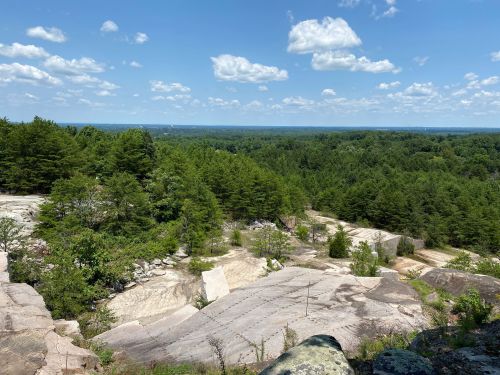 A scenic view of rocky terrain and lush green trees under a blue sky with fluffy clouds.