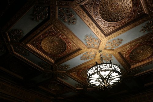Ornate ceiling with intricate gold designs and a vintage chandelier in the center, creating an elegant atmosphere.