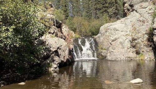A serene waterfall cascades into a calm pool, surrounded by rocky terrain and lush greenery.