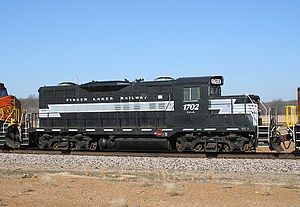 A black and white locomotive labeled "1702" parked on railway tracks under a clear blue sky.