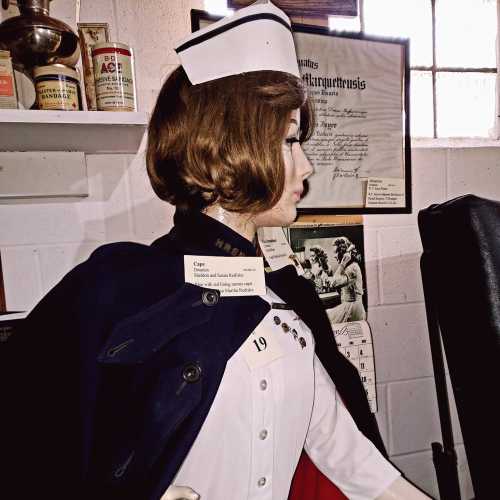 A vintage mannequin dressed as a nurse, wearing a cap and cape, displayed in a museum setting.