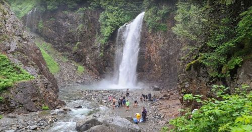 A scenic waterfall cascades down rocky cliffs, with people exploring the area and enjoying the natural beauty.