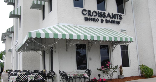 Exterior of Croissants Bistro & Bakery featuring a striped awning and outdoor seating with tables and chairs.