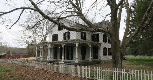 A large, white Victorian-style house with black shutters, surrounded by a picket fence and bare trees.