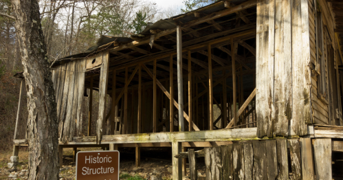 An old, weathered wooden structure with a sign reading "Historic Structure" in a forested area.