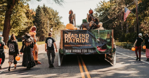 A group of people walks towards a trailer advertising "The Dead End Hayride," with Halloween decorations and pumpkins.