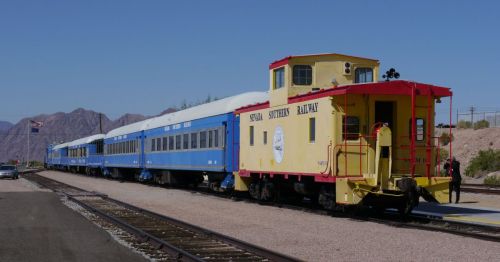 A yellow caboose and blue train cars parked on a railway track with mountains in the background.