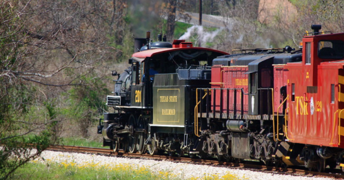 A vintage steam locomotive with a black and red color scheme, traveling along a scenic railway track.