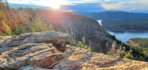 Sunset over a scenic landscape with rocky outcrops, trees, and a winding river in the distance.