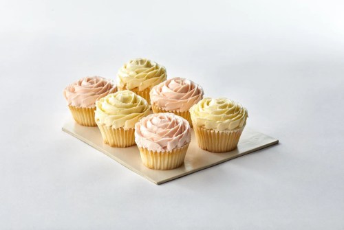 A plate of six cupcakes with swirled frosting in pink and yellow colors, arranged neatly on a white background.